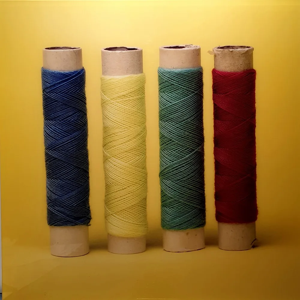 Bobinas de hilo en azul, amarillo, verde y rojo sobre fondo amarillo, fotografía de Jordi Puig