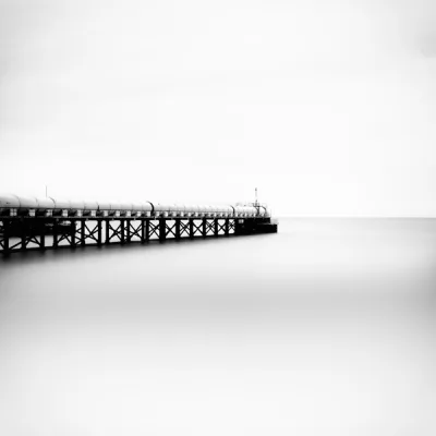 Fotografía en blanco y negro de un muelle que se extiende hacia el horizonte, obra de Kike Suay titulada El tubo